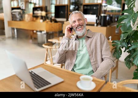Happy mature business man sitting in cafe talking on phone making call. Stock Photo