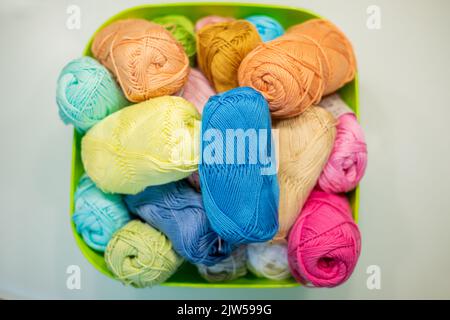 Multi-colored bright yarn lies in a box on a white table, selective focus. Stock Photo