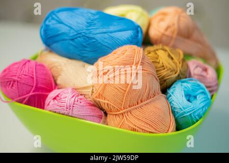 Multi-colored bright yarn lies in a box on a white table, selective focus. Stock Photo