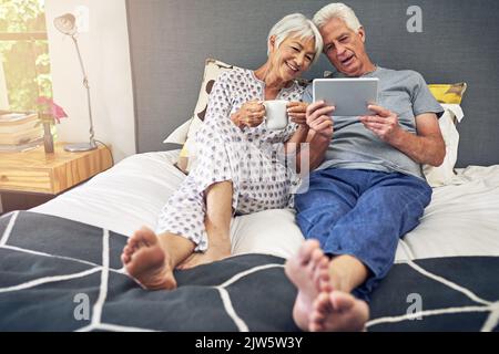 Home is where your heart is. a senior couple using a tablet while lying in bed. Stock Photo