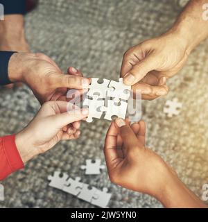 Putting it all together. High angle shot of four unrecognizable businesspeople building a jigsaw puzzle. Stock Photo