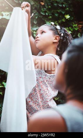 Teach kids responsibility by getting them involved in chores. a mother and her little daughter hanging up laundry on a washing line outdoors. Stock Photo