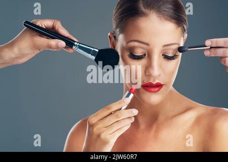 Beauty in creation. Studio shot of a beautiful young woman getting her makeup done against a grey background. Stock Photo