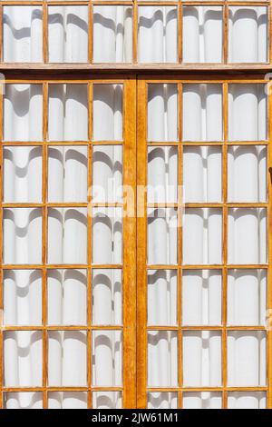 Wooden lattice of panoramic window on sunny day with closed white curtains. Empty huge floor-to-ceiling window on entire wall, no one, interior space Stock Photo