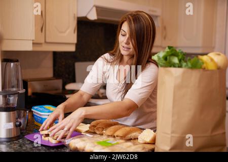 Preparing a delicious meal. a young woman making sandwiches in a kitchen. Stock Photo