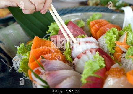 Closeup tako picking with chopsticks from mix sashimi set in ceramic plate. Japanese Cuisine Buffet. Chef's Choice: Salmon, hamachi, Tako, Hotate and Stock Photo