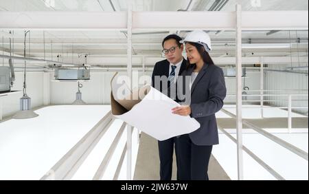 Engineer in hardhat hold the ventilation system construction plan while taking the building inspector check the cleanliness of the factory. lighting a Stock Photo