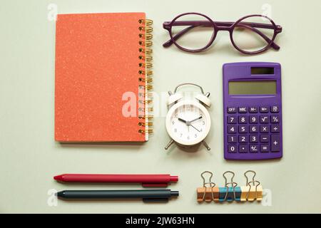 Office desk table with notebook, eyeglasses, clock, clip, calculator, pen, supplies on green desk. flat lay, top view, copy space Stock Photo