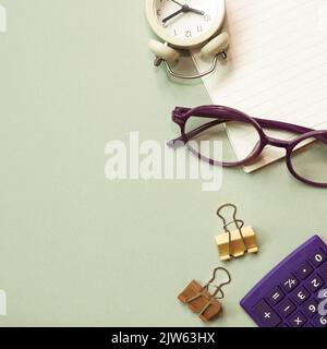 Office desk table with notebook, eyeglasses, clock, clip, calculator, supplies on green desk. flat lay, top view, copy space Stock Photo