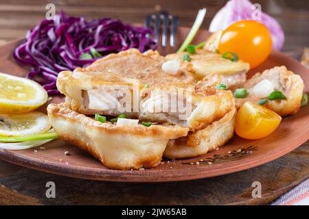 Juicy, flavorful, healthy food. Front and close view of several pieces of fish battering with yellow cherry tomatoes, lemon, garlic, leek and red cabb Stock Photo