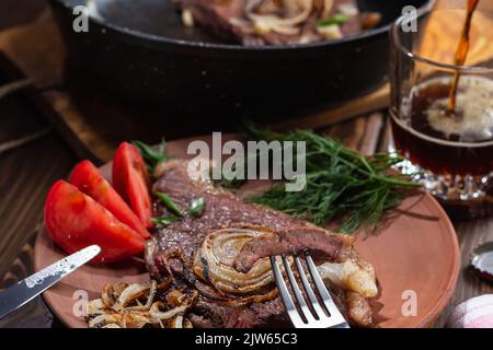 Two fried beef steaks.Focus on piece of meat strung on fork, beer poured into glass, selective focus.Healthy food concept. Stock Photo