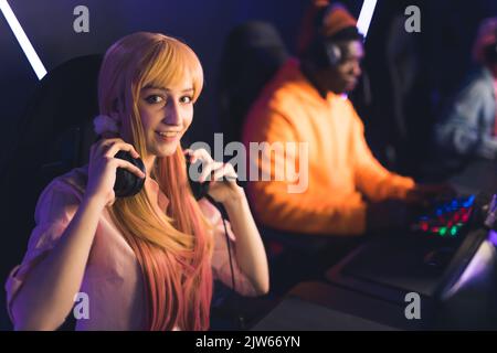 Young asian woman with cute dyed pigtails holding headset around neck playing online game with friends looking into the camera smiling. Horiontal shot. High quality photo Stock Photo