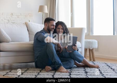 Millennial couple using digital tablet seated on floor at home Stock Photo