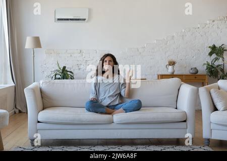 Attractive Hispanic woman holds remote controller turns on AC Stock Photo