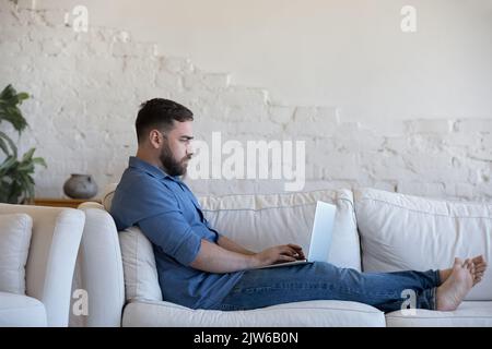 Serious freelancer sit on sofa working remotely on laptop Stock Photo