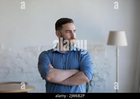 Serious pensive man standing indoor staring into distance Stock Photo