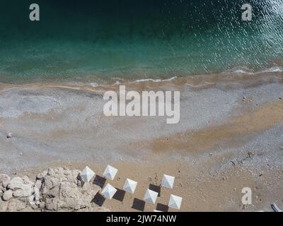 Aerial view from above on azure sea and pink pebbles beach. Small waves on cristal clear water surface in motion blur. Summer ocean sea beach Stock Photo
