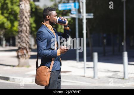 African american man standing using smartphone and drinking coffee Stock Photo