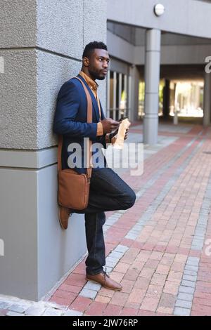 African american man standing using smartphone and eating a croissant Stock Photo