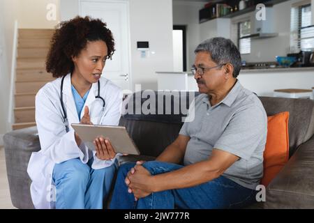 Senior mixed race man with female doctor home visiting talking using tablet Stock Photo