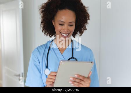 Mixed race female doctor home visiting using tablet and smiling Stock Photo