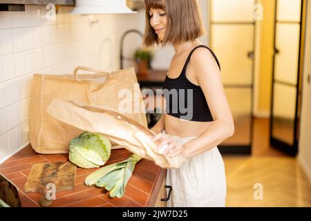 Woman unpacks freshly bought vegetables on kitchen table Stock Photo