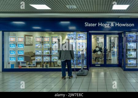 Single senior man looking at properties in the window of an estate agents in The Centre shopping mall in Cumbernauld New Town. Stock Photo