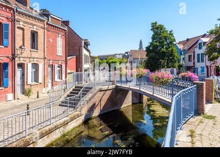 Typical brick townhouses line the Somme river in the Saint-Leu historic district in Amiens, France, with a footbridge on a sunny summer day. Stock Photo