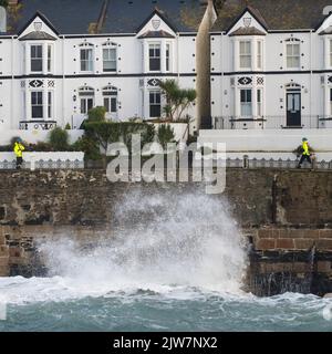 Coastguards standing by to stop people getting washed in by big waves smashing in Porthleven harbour along Bay View terrace Stock Photo