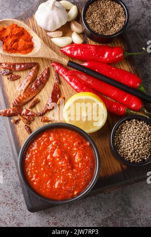 Harissa Paste North African spicy red sauce to add heat to dressings, sauces, soups in bowl on wooden board with ingredients closeup. Vertical top vie Stock Photo
