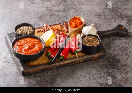 Hot chilli pepper sauce paste harissa, Arabic cuisine adjika on the bowl on wooden board with ingredients closeup. Horizontal Stock Photo