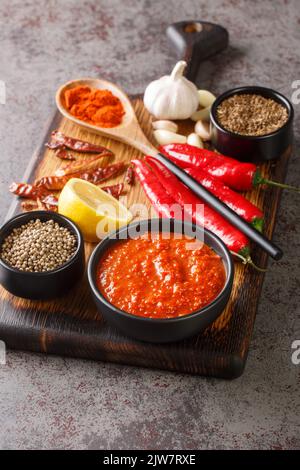 Harissa Paste North African spicy red sauce to add heat to dressings, sauces, soups in bowl on wooden board with ingredients closeup. Vertical Stock Photo