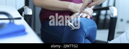 Doctor neurologist knocking on knee of patient with hammer in clinic closeup Stock Photo