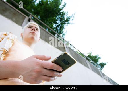 boy seen from below holding a cell phone in the foreground Stock Photo