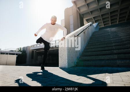 Fit urban guy performing a wall spin outdoors in city. Young sportsman practicing parkour and free running. Stock Photo