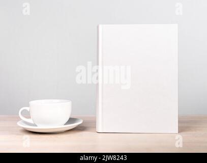 Book mockup and cup at wooden table. Reading leisure, relaxation with tea or coffee mug, harmony concept. Novel, encyclopedia, code template with empt Stock Photo
