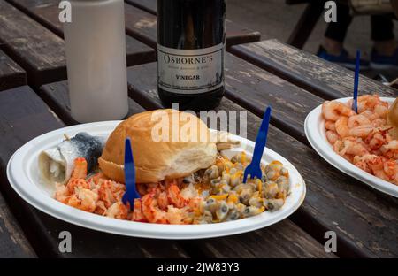 A plate of seafood with cockles, crayfish, a rollmop and anchovies at the long established Osbourne Bros on the quayside at Leigh-on-Sea, Essex, UK. Stock Photo