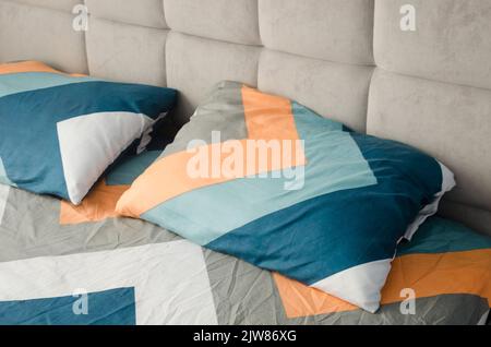 Close up shot of colorful yellow and blue geometric pattern pillows on grey bed in modern bedroom in stylish room interior. Cozy concept. Stock Photo