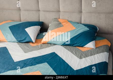 Close up shot of colorful yellow and blue geometric pattern pillows on grey bed in modern bedroom in stylish room interior. Cozy concept. Stock Photo