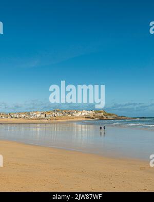 Couple taking a long walk at low tide on Porthminster beach towards St Ives harbour. Stock Photo