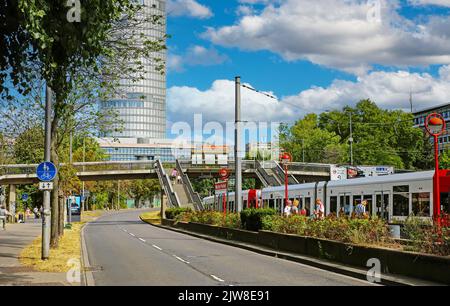 Cologne (Deutzer Freiheit), Germany - July 9. 2022: Street in city center, subway station, train, triangle tower, pedestrian crossing bridge, blue sum Stock Photo