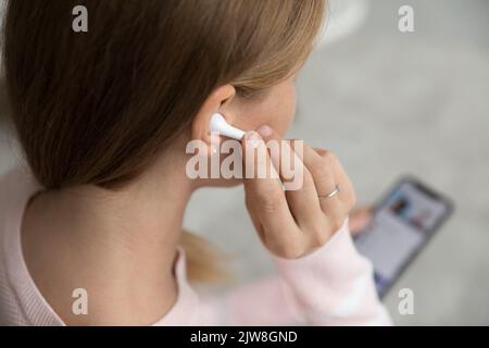 Young Caucasian gadget user woman touching wireless earphone in ear Stock Photo