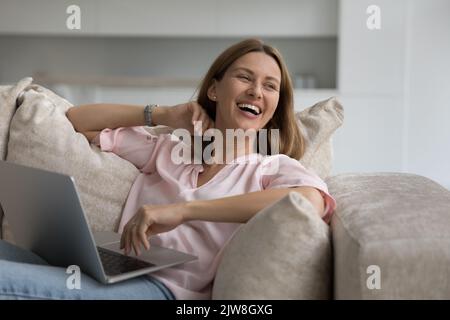 Cheerful freelancer woman working on home couch, holding laptop Stock Photo
