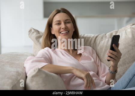Cheerful beautiful 30s Caucasian woman holding smartphone, looking at camera Stock Photo