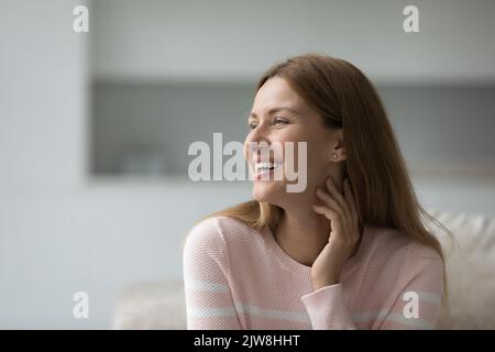 Happy dreamy pretty 30s woman in casual sitting on couch Stock Photo