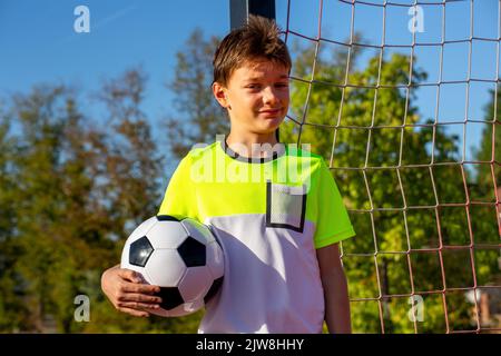 Symbol image: Ten-year-old boy on a football pitch proudly holding a football in his arms (model released) Stock Photo