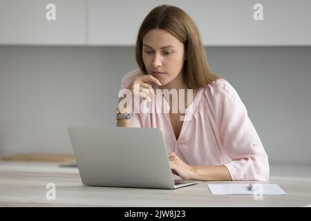 Focused thoughtful freelance employee woman working in home kitchen Stock Photo
