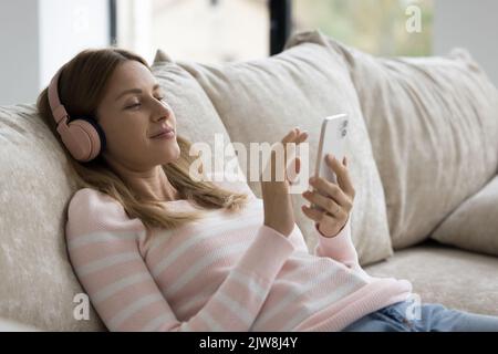 Relaxed smartphone user woman in wireless headphones listening to music, Stock Photo