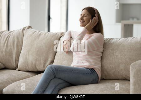 Positive woman in big wireless headphones sitting on home sofa Stock Photo
