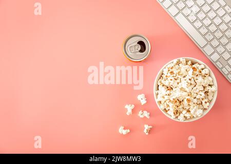 A bowl of popcorn, a keyboard and a can of drink on a pink background. Stock Photo